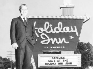 A Man Standing In Front Of A Sign Posing For The Camera